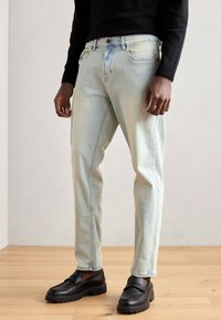Light blue denim jeans featuring a straight-leg design, slight fading, and a five-pocket style. Paired with black slip-on shoes.