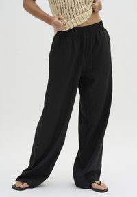 Zwarte wijde broek gemaakt van lichte stof met een elastische tailleband en verstelbaar trekkoord, met een gladde textuur en eenvoudig ontwerp.