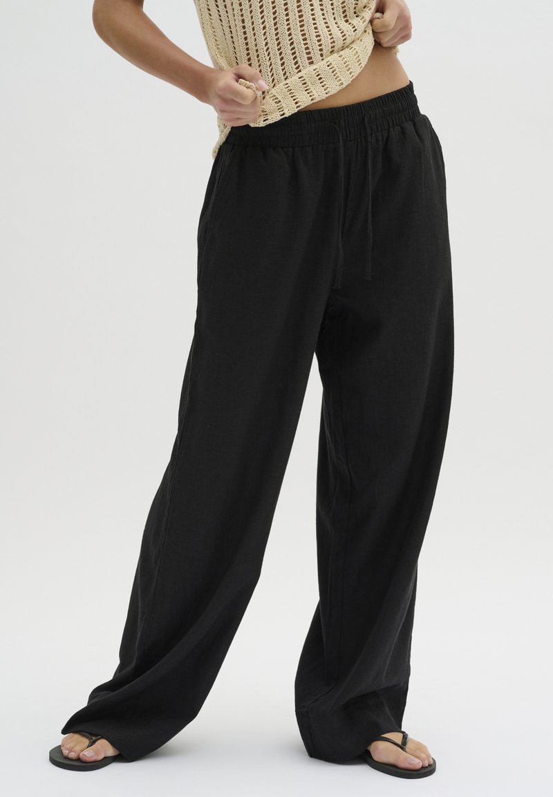 Zwarte wijde broek gemaakt van lichte stof met een elastische tailleband en verstelbaar trekkoord, met een gladde textuur en eenvoudig ontwerp.
