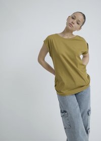 Senapsgul, kortärmad topp med avslappnad passform, tillsammans med ljusblå, vida jeans med cargofickor. Slät textur.