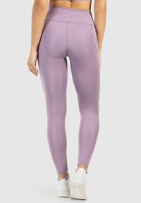 Leggings a vita alta in lavanda, realizzati in tessuto elasticizzato con una texture liscia e tasche laterali, abbinati a sneakers sportive bianche.