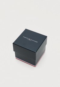 Tommy Hilfiger watch box, dark blue cardboard with a red and white accent at the base, featuring the brand's logo on the lid.