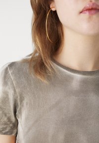 Olive green ribbed T-shirt with a round neckline, featuring a soft texture. Large gold hoop earring visible in the ear.
