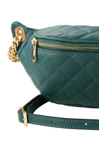 Gequilte groene leren heuptas met gouden rits en hardware, voorzien van een kettingaccent en een verstelbare band.