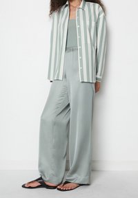 Camisa de botones a rayas verde claro, top de tirantes verde sólido a juego y pantalones anchos de satén. Sandalias negras completan el look.