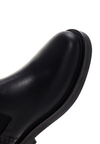Botte Chelsea en cuir lisse noir avec bout arrondi, panneau latéral élastique et semelle épaisse en caoutchouc sur fond blanc.