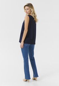 Tumesinine ilma varrukateta särk, millel on aukudega disain, koos siniste laienevate teksade ja heleda beeži kontsaga. Sile tekstuur, mugav lõige ja kihiline välimus.