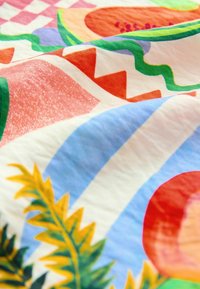 Farebný textil s abstraktnými tvarmi v ružovej, červenej, modrej a zelenej farbe, so tropickými listovými akcentmi a geometrickými vzormi.
