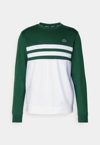 Grön och vit sweatshirt med långa ärmar, med tre horisontella ränder och en Lacoste-logotyp på bröstet. Tillverkad av bomull.