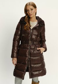 Hnědý péřový kabát s kožichem, zipem vpředu, páskem v pase a bočními kapsami. Obsahuje horizontální prošívaný vzor a lesklou texturu.