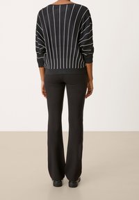 Czarny sweter z pionowymi białymi paskami, luźny krój i ściągacze; w połączeniu z czarnymi spodniami dzwonami i masywnymi czarnymi butami.