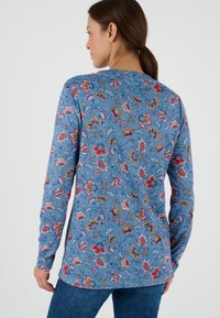 Camicia a maniche lunghe floreale realizzata in tessuto leggero, con uno sfondo blu e motivi di fiori colorati, dotata di orlo dritto.