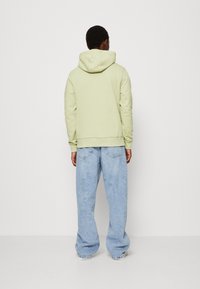 Ljusgrön huvtröja med känguruficka, mjuk textur och dragsko i huvan, tillsammans med löst sittande ljusblå denimjeans.