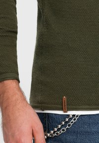 Olijfgroen gestructureerd sweater met lange mouwen, voorzien van een geweven patroon, platte gebreide manchetten en een bruin labelaccent nabij de zoom.