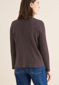 Pitkähihaisen tumman violetin ja valkoisten raitojen paita, tiukka malli pyöreällä kaula-aukolla, pehmeä kangas, yhdistettynä sinisiin farkkuihin.