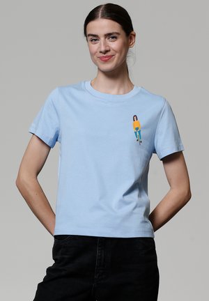 T-shirt en coton bleu clair à manches courtes, avec un petit graphique coloré représentant un personnage à vélo sur la zone gauche de la poitrine.