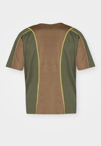T-shirt de manga curta castanho e verde com painéis em contraste e costura amarela ao longo das costuras. Textura de tecido suave.