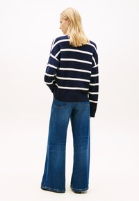 Πλεκτό πουλόβερ με ναυτικό ριγέ σχέδιο και λευκές οριζόντιες ρίγες. Συνδυασμένο με πλατύτερα τζιν παντελόνια σε μπλε χρώμα, με πίσω τσέπες και ξεφτισμένο τελείωμα.