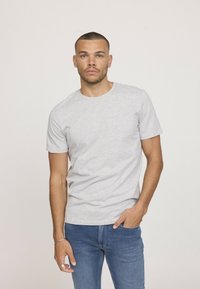 T-shirt gris à manches courtes en coton doux, avec un col rond et un design simple et épuré. Assorti à un jean bleu.