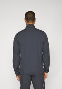 Navyblå lett jakke med stående krage, elastiske mansjetter og hem. Stoffets tekstur ser glatt ut uten synlige mønstre eller hardware.