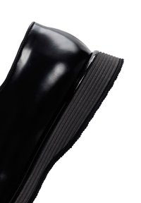 Botte de cheville noire brillante avec une semelle en caoutchouc épaisse et nervurée. La tige est en cuir lisse avec un design à bout arrondi.