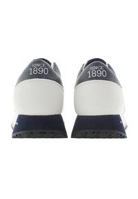 Herrskor i sneakersstil med en marinblå och vit färgpalett, med en stilren design, slätt läder och gummisulor. "Sedan 1890" tryckt på baksidan.