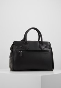 Borsa in pelle nera con doppi manici, tasca frontale con zip e design minimalista, posizionata su un piedistallo bianco su sfondo neutro.