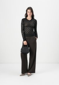 Haut à manches longues en dentelle noire avec un motif floral, associé à un pantalon taille haute à jambes larges brun. Tenant un petit sac à main en cuir texturé noir.
