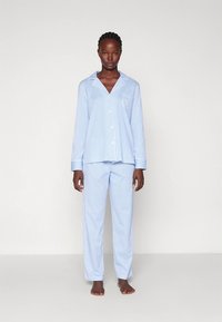 Σετ πυτζάμας με μπλε και λευκές ρίγες που περιλαμβάνει επάνω μέρος με κουμπιά και γιακά, καθώς και παντελόνι που ταιριάζει, κατασκευασμένο από ελαφρύ ύφασμα.