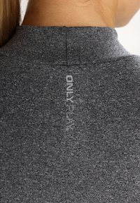 Top grigio, con texture morbida e colletto alto, caratterizzato da un motivo sottile. Il logo del marchio "ONLY" è stampato verticalmente sul retro.