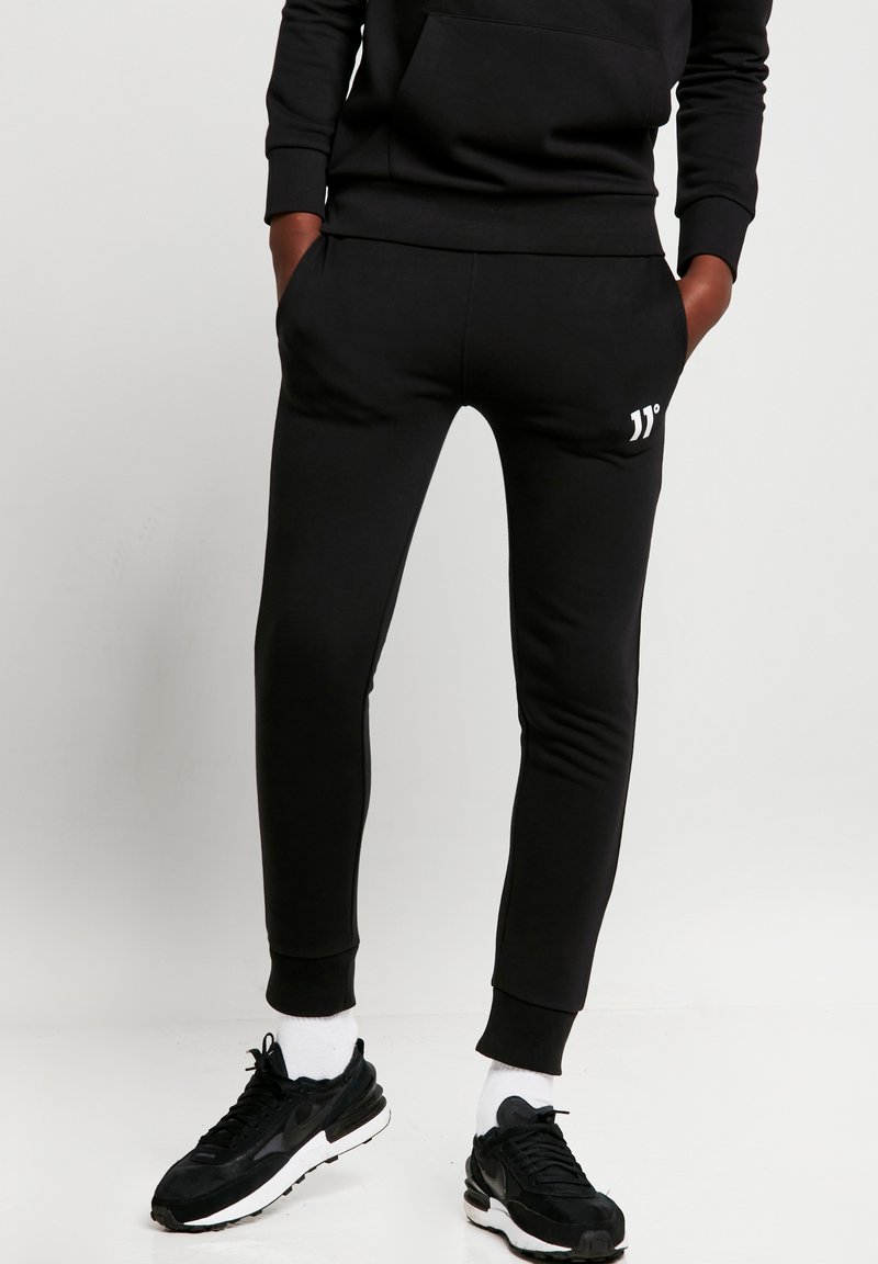 Pantalones de chándal negros hechos de una tela suave con un corte ajustado, que cuentan con bolsillos laterales y un pequeño logo blanco cerca de la cintura.