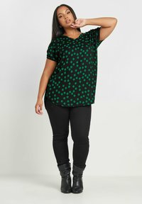 Mustat paita, jossa on vihreitä viiruja, lyhyet hihat ja V-kaula-aukko. Yhdistetty tiukkoihin mustiin farkkuihin ja mustiin nilkkakorkoihin.