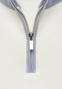 Nahaufnahme eines silbernen Reißverschlusses, der teilweise geöffnet ist, auf einem hellen Strickstoff mit hellblauem Saum.