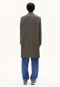 Grau melierter Wollblenden-Mantel mit gerader Silhouette, Rückenschlitz und langen Ärmeln, kombiniert mit lockeren blauen Denimhosen und Sneakers.