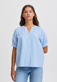 Blusa a righe azzurro chiaro con maniche a sbuffo corte, chiusura frontale a bottone e scollatura rotonda. Il tessuto morbido e le righe verticali creano una vestibilità rilassata.