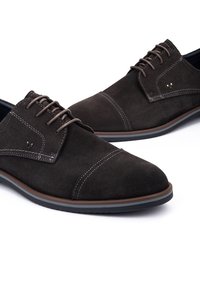 Zapatos de ante marrón oscuro con un diseño de cordones, costuras contrastantes y suela de goma. Presentan puntera cap y un acento de hardware minimalista.