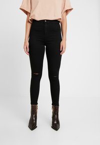 Svarta skinny jeans med framåtrivna hål, hög midja, i kombination med ankellånga bruna stövlar med ormskinnsmönster.