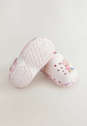 Lyserøde træsko med sål i blomsterprint, ventilationshuller og en dekorativ kaninudsmykning foran. Mønstret gummiydersål.