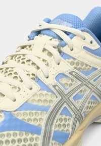 Αθλητικό παπούτσι σε ανοιχτό καφέ και μωβ μπλέ υλικό με διαμορφωμένο σχέδιο, ευέλικτο υλικό και στρογγυλά κορδόνια. Διαθέτει λογότυπο στη γλώσσα του.