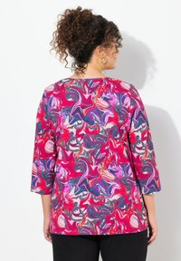 Kleurige, gemarmerde blouse met roze, rode en paarse wervelingen. Lange mouwen en een ronde halslijn. Gekocht in combinatie met zwarte broek.
