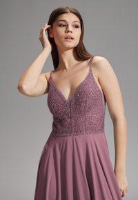 Robe longue et fluide en mauve clair avec un corsage perlé et scintillant. Dotée d'un décolleté en V profond et de fines bretelles. Jupe douce et texturée.