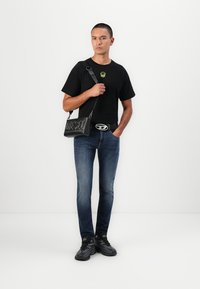 T-shirt noir avec un col rond, jean foncé et baskets noires. Comprend un sac bandoulière noir avec logo "DIESEL" en relief et quincaillerie argentée.