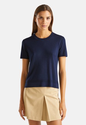 Navyblauwe gebreide trui met korte mouwen, ronde halslijn en een rechte zoom, gecombineerd met een beige geplooide rok. Zachte textuur, casual pasvorm.