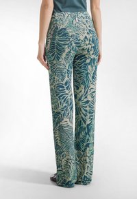 Leveälahkeiset housut, jotka on valmistettu kuvioidusta vihreän ja beigen sävyisestä kankaasta, jossa on lehtikuvio. Housuissa on korkeavyötärö ja sileä pinta.