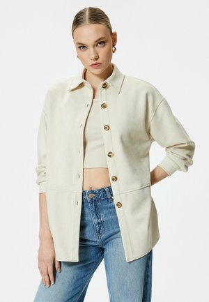 Cremefarvet oversized skjortejakke med krave, knaplukning foran og ribbede manchetter. Båret sammen med højtaljede blå jeans.