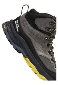 Scarpa da trekking con tomaia grigia e nera in tessuto a rete e scamosciato, suola Vibram con accenti gialli e lacci neri.