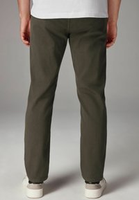 Pantalones ajustados de un verde oscuro, fabricados en una tela suave con una textura lisa. Cuentan con bolsillos estándar y se combinan con zapatillas blancas.
