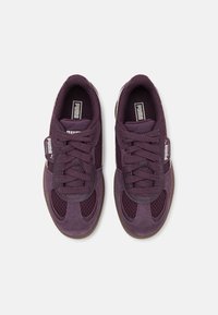 Ett par mörk lila Puma Palermo-sneakers med nät- och mockapaneler, snörda, sedda ovanifrån på en vit bakgrund.