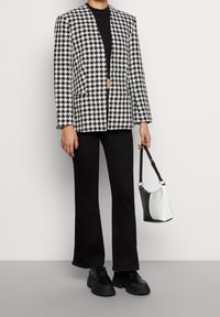 Sort og hvid houndstooth blazer med klapper, parret med sorte vide bukser og en to-farvet håndtaske i sort og hvid. Sorte sko.