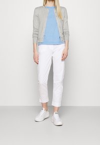 Grå cardigan, ljusblå t-shirt och vita cropped byxor. Vita sneakers med texturerade sulor. Enkelt, figursydd design, lämplig för avslappnad klädsel.